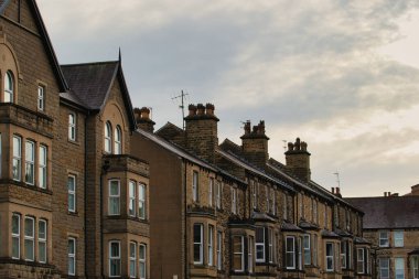 Teraslı evler, ağırlıklı olarak kahverengi taşlar, değişik sayıda pencere ve bacalar, bulutlu bir gökyüzünün altında. Harrogate, İngiltere 'de mimari tarzı tutarlı..