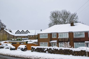 Karla kaplı evler ve arabalar. İngiltere 'nin Harrogate kentindeki taş duvar ve diğer karla kaplı binaların yanındaki odak noktası, iki katlı, karla kaplı bir tuğla ev..