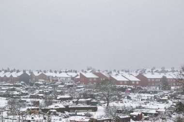 Karla kaplı banliyö evleri ve bulutlu bir günde uzaktan izlenen tahsisatlar. Sahneye kırmızı tuğlalı evler hakim olurken, Harrogate, İngiltere 'de daha küçük barakalar ve bahçe yapıları ön planda görülebilir..