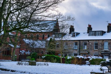 Bir kilise ve teraslı evler de dahil olmak üzere karla kaplı tuğla ve taş binalar kışın bir parktan görülürler. Harrogate, İngiltere 'de büyük çıplak bir ağaç ön plana hakim..