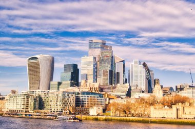 Nehrin karşısındaki Londra gökdelenleri, Walkie-Talkie gibi modern gökdelenlerin yanı sıra daha eski, alçak binaların yanı sıra tarihi bir taş yapının bir kısmının da yer aldığı bir gökdelenle çevriliydi. Pofuduk bulutlu mavi gökyüzü.