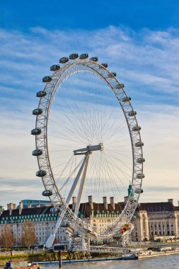 Londra Göz Dönme dolabı görüntüye hükmediyor. Kapsülleri berrak mavi gökyüzüne karşı görülebilir. Binalar arka plandaki nehir kıyısına dizilir..