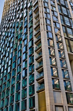 Yüksek binalarda çok sayıda balkon ve deniz mavisi çerçeveli pencereler bulunur. Binanın dışı açık bej renkte, pencere ve balkonların oluşturduğu ızgara benzeri bir desen var. Perspektif Londra, İngiltere 'de düşük açılı bir çekim..