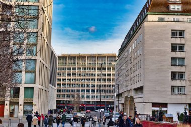 İki modern ve bir yüzyılın ortasında parçalı bulutlu bir gökyüzünün altında üç çok katlı binalı bir şehir caddesi manzarası. Yayalar Londra, İngiltere 'deki binalar arasında cadde boyunca yürüyorlar..