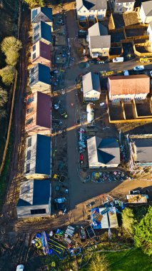 Konut inşaatı alanının havadan görüntüsü. Çeşitli tamamlama aşamalarında birden fazla ev, inşaat malzemeleri ve malzemelerle birlikte görülebilir durumda. Sahne, Knaresborough 'da öğleden sonra güneşinden gelen dünyevi tonlar ve gölgelerle dolu.