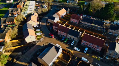 Aerial view of a new housing development.  Rows of two-story houses with red tile roofs are prominent, along with surrounding roads, undeveloped land, and other buildings.  Construction is ongoing in some areas in Knaresborough, UK. clipart