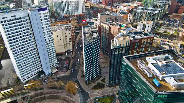 Belirgin beyaz gökdelenler, koyu camlı modern binalar ve tuğla yapılar da dahil olmak üzere çeşitli mimari stil ve renklere sahip çok sayıda yüksek binaların yer aldığı bir şehir bloğunun havadan görünüşü. Sokak seviyesinde arabalar, otobüsler ve yayalar var 