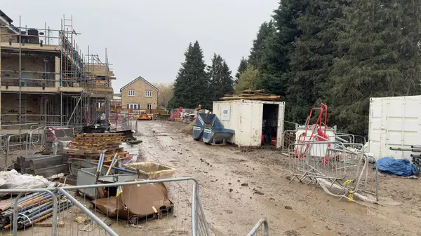 Kısmen inşa edilmiş evler, iskeleler, inşaat malzemeleri ve nakliye konteynırları olan çamurlu bir inşaat alanı. Çamurun içinde çeşitli araç ve gereçler var..