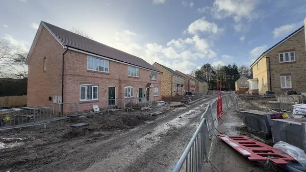 Çamurlu bir sokakta yeni inşa edilmiş tuğla evler, hala yapım aşamasında. Geçici eskrim ve inşaat enkazı görülebilir durumda. Gökyüzü parçalı bulutlu.