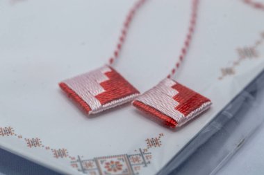 Kırmızı ve pembe işlemeli iki küçük kare yama yakın çekim, ince kırmızı ipliklere bağlı, beyaz, nakışlı bir yüzey üzerinde dinleniyor.