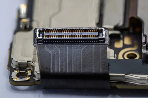 Siyah, esnek bir devre kartına bağlı sayısız lobutu olan altın kaplamalı bir konnektörün yakın çekimi. Bağlantı merkezi olarak metalik bileşenleri olan daha büyük bir devre kartının üzerine yerleştirilmiştir..