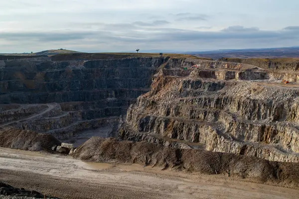 Açıkta kaya tabakası olan büyük, teraslı bir taş ocağının havadan görünüşü. Çamurlu yollar ve toprak yığınları görülebilir. Ağır makineler mevcut.
