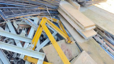Paslı metal iskelet, ahşap kalaslar ve çeşitli metal bileşenler de dahil olmak üzere karışık inşaat enkazı yığını. Sarı metal çerçeve öne çıkıyor..