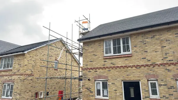 İki bitişik tuğla ev yapım aşamasında. Bir ev iskeleye sahipken, diğeri büyük oranda eksiksiz. Her ikisi de tuğla, pencere ve çatı işçiliğini gösteriyor.