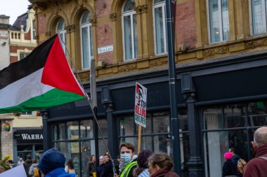 Kalabalığı gösteren bir sokak fotoğrafı, bir Filistin bayrağı ve binaların önünde 