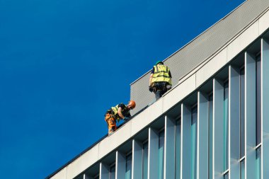 Manchester, İngiltere 'de açık mavi gökyüzüne karşı modern bir binanın çatısında iki inşaat işçisi..