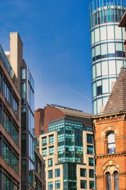 Değişik mimari tarzları ve yükseklikleri gösteren bir bina koleksiyonu, Manchester, İngiltere 'de açık mavi gökyüzüne karşı sergilenmektedir..