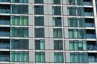 Pencereleri ve balkonları olan modern bir apartman cephesine yakın plan. Manchester, İngiltere 'de ağırlıklı olarak gri, siyah ve mavi-yeşil renkler..