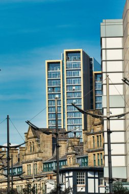 Kentsel manzara: Geleneksel mimarinin arkasındaki modern yüksek binalar, berrak mavi bir gökyüzünün altında. Manchester, İngiltere 'de sokak lambaları.