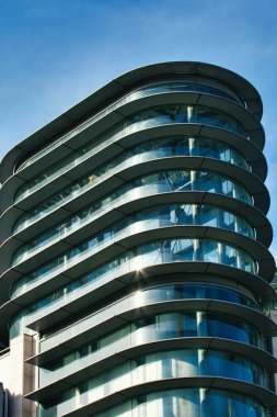 Manchester, İngiltere 'de açık mavi gökyüzüne karşı cam pencereler ve metal çerçeveli modern, eğimli bir binanın alçak açılı görüntüsü..