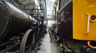 İki lokomotifin olduğu bir iç çekim, biri eski siyah buhar makinesi, diğeri de kahverengi ve sarı dizel motor, National Railway Museum York 'ta karşı karşıya..