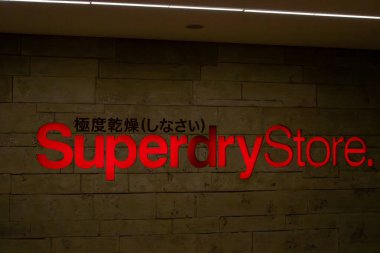 Kırmızımsı neon harflerle yazılmış kahverengi tuğla bir duvarda süperkuru bir tabela. Markanın üzerindeki Japonca metin.