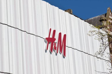H & M mağazasının dış görüntüsü. Beyaz kıvrımlı cephede kırmızı logo. Liverpool, İngiltere 'de açık mavi gökyüzü.