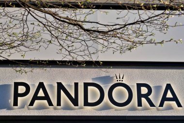 Harrogate, Yorkshire, İngiltere 'de ön planda dalları ve tomurcuklanan yaprakları olan beyaz desenli bir duvarda pandora işareti..