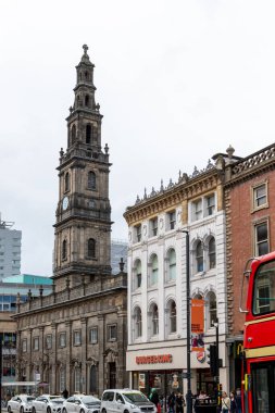 Uzun bir kilise kulesi, bitişik binalar, yayalar, araçlar ve Leeds, İngiltere 'de bulutlu bir gökyüzünün altında Burger King restoranı olan şehir manzarası..