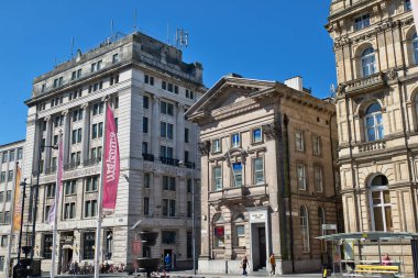 Liverpool, İngiltere 'de açık mavi bir gökyüzü altında, insanlar ve sokak mobilyaları ile Ulusal Banka da dahil olmak üzere çeşitli binaların dış görüntüsü..