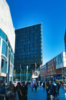 Liverpool, İngiltere 'de birçok yayanın önünden geçtiği, berrak mavi gökyüzünün altında, uzun camdan bir kule de dahil olmak üzere modern binaların bulunduğu şehir manzarası..