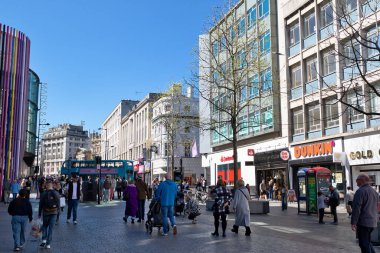 Ticari bir cadde boyunca yürüyen yayaların olduğu sokak sahnesi. Bina iki taraftan da kuşatıldı ve Liverpool, İngiltere 'de mavi bir gökyüzü var..