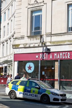 Bir polis arabası Pret A Manger 'ın önüne park edilmiş. İnsanlar yakınlarda yürüyorlar. Bina Liverpool, İngiltere 'de açık renkli taştır..