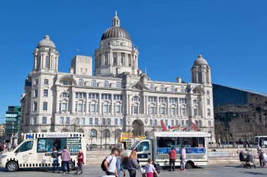 İngiltere, Liverpool 'da açık mavi gökyüzü altında büyük, süslü bir bina yiyecek kamyonları ve önplanda insanlar var..