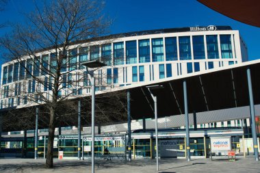 Bir otobüs durağının arkasında solunda çıplak bir ağaç ve Liverpool, İngiltere 'de parlak mavi gökyüzü olan Hilton Oteli' nin dış görüntüsü..