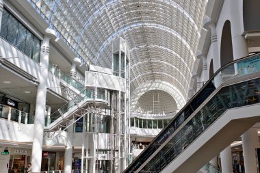 Cam çatılı bir alışveriş merkezinin iç manzarası, yürüyen merdivenler, asansör ve çok katlı mağazalar. Kingston, İngiltere 'deki Bentall Merkezi' nde çoğunlukla beyaz ve cam mimari unsurlar var..