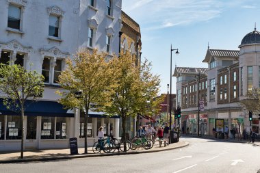 Wimbledon, Londra 'da güneşli bir günde kaldırım boyunca park etmiş binalar, ağaçlar, insanlar ve bisikletlerin olduğu sokak manzarası..