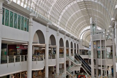 Görüntü, Kingston, İngiltere 'deki Bentall Center' da birden fazla katlı, beyaz sütunlu, kemerli, dükkanlı, yürüyen merdivenli ve cam çatılı bir alışveriş merkezinin içini gösteriyor..