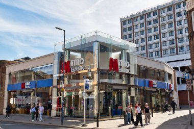 Şehir caddesinde yayalarla dolu bir Metro Bank şubesinin dış görüntüsü. Kingston, İngiltere 'de mavi tabela ve cam cephe görünür..
