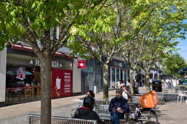 Sokak manzarasında ağaçlar, banklar, mağazalar, insanlar ve bir bisiklet var. Kingston, İngiltere 'de parlak güneş ışığı.