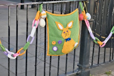 Örülmüş Paskalya süslemeleri siyah metal bir çitten sarkıyor, içlerinde tavşan çantası, örgü yumurtalar ve Ripon, Yorkshire, İngiltere 'de renkli bir örgülü zincir de var..