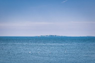 Deniz feneri, tekne ve parlak bir gökyüzünün altındaki sularda bulunan birkaç martıya ev sahipliği yapan bir ada..
