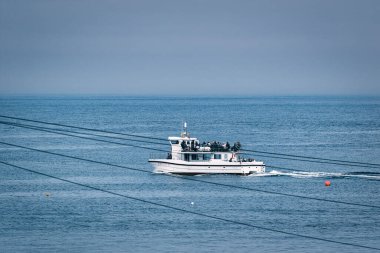 Beyaz yolcu gemisi mavi sularda yol alıyor, yolcu taşıyor. Kablolar ve şamandıralar da İngiltere 'deki Deniz Evleri Limanı' nda görülebilir durumda.