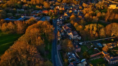 İngiltere 'nin Knaresborough kentindeki altın güneş ışığıyla aydınlatılmış, içinden geçen bir yol, evler ve ağaçların bulunduğu bir kasabanın havadan görünüşü..