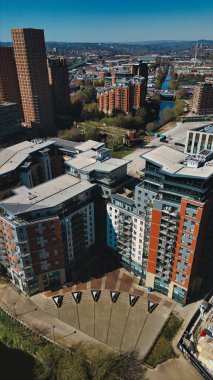 Güneşli bir günde açık mavi bir gökyüzü altında, Leeds, İngiltere 'de bir kanal ve şehir manzarasına sahip modern apartman binalarının ve kentsel manzaranın havadan görüntüsü..