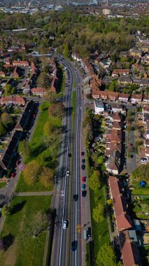 Morden, Londra, İngiltere 'de evleri ve ağaçları olan bir banliyö bölgesinden geçen arabalı bir yolun hava görüntüsü..