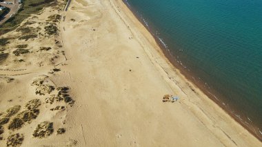 Kum tepeleri ve okyanusla birleşen kumlu bir sahil manzarası. İnsanlar kumsala ve Sandhaven Sahili 'ndeki suya dağılmış durumda..