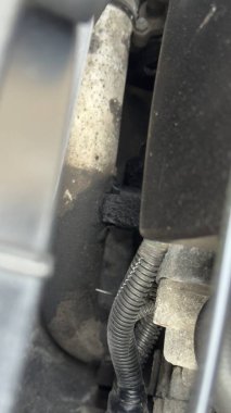 Motor kompartımanının yakın görüntüsü. Hortumlar, kablolar, motor parçaları, hepsi görünür toprak ve aşınmış..