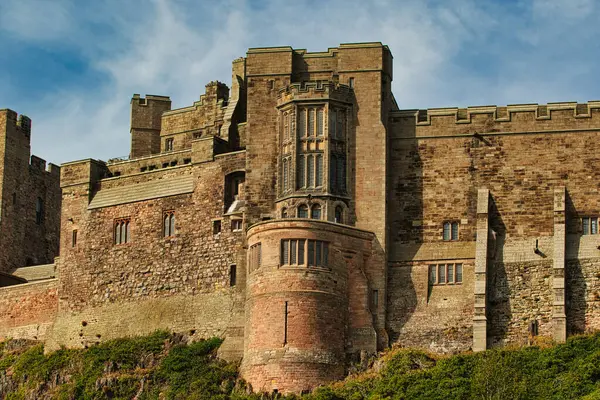 Büyük, heybetli taş bir kale. Birden fazla kulesi, duvarları ve penceresi var. Bamburgh Şatosu 'ndaki üste yeşil bitki örtüsü..