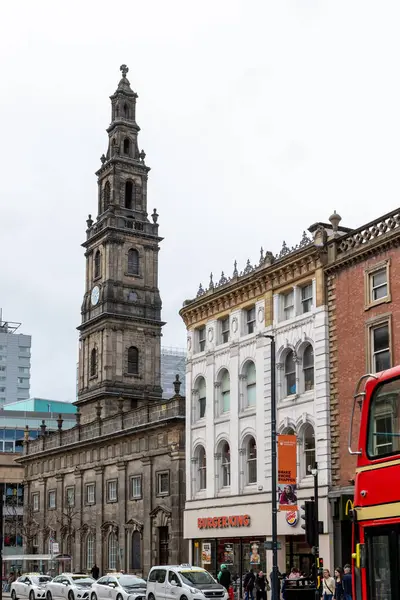 Uzun bir kilise kulesi, bitişik binalar, yayalar, araçlar ve Leeds, İngiltere 'de bulutlu bir gökyüzünün altında Burger King restoranı olan şehir manzarası..
